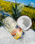 Bottle of Street Party Spirit Co. Coconut Rum with a pineapple and half a coconut on shreds of coconut in a field.